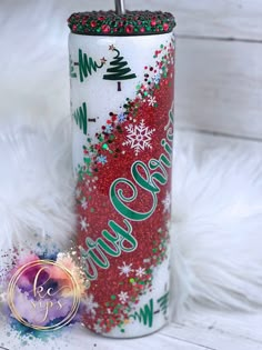 a red and green christmas tumbler next to a white fur background with the words merry written on it