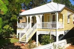 a yellow house sitting next to a white picket fence and trees in front of it