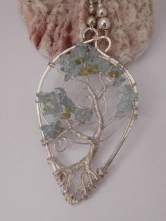 a tree of life pendant with green and blue beads on a white surface next to a rock