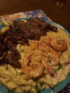 a blue plate topped with pasta covered in meat and shrimp next to veggies