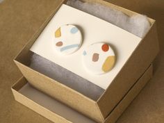 two buttons in a box on top of a cardboard box with white and yellow designs