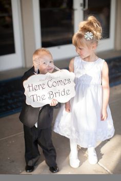 two young children dressed in formal wear holding a sign that says here comes the bride