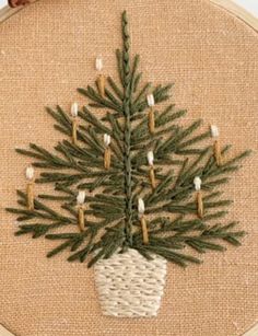 a cross stitch christmas tree on a burlock with candles in the shape of a pine cone