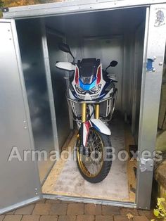 a motorcycle is parked in a small metal storage shed on the side of a road