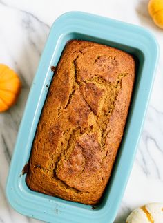 a loaf of pumpkin bread sitting in a blue dish on a marble counter top next to mini pumpkins