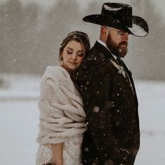 a bride and groom are standing in the snow wearing black hats, scarves and coats