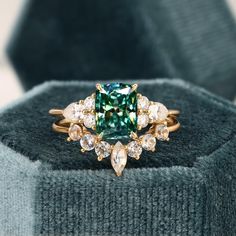 a ring with an emerald colored stone surrounded by white and brown diamonds on top of a gray sweater