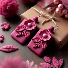 two pink flower shaped earrings sitting on top of a table next to a brown box