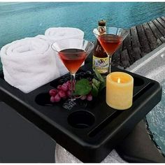 two glasses of wine on a tray with towels and candles next to the water in front of them