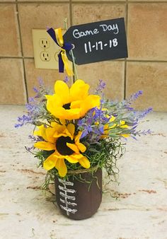 a vase filled with yellow and purple flowers next to a sign that says game day