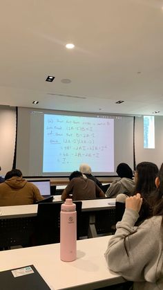 people sitting at desks in front of a projector screen with writing on it