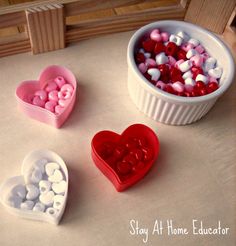 three heart shaped containers filled with hearts on top of a white countertop next to a cup full of candy