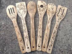 four wooden utensils are lined up in a row on the ground with flowers drawn on them