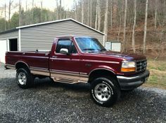 a maroon pick up truck parked in front of a house with a shed behind it