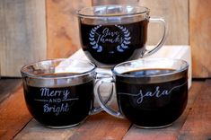 three coffee mugs with merry and bright written on the cups are sitting on a wooden table