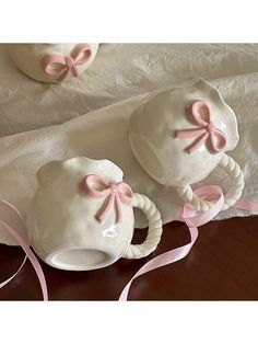 two white ceramic teapots with pink bows on them