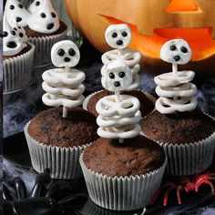 cupcakes decorated with white frosting and spooky eyes are sitting in front of a pumpkin