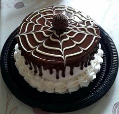 a chocolate cake with white frosting and spider web decoration on top, sitting on a black plate