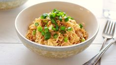 a bowl filled with noodles and green onions on top of a table next to silverware