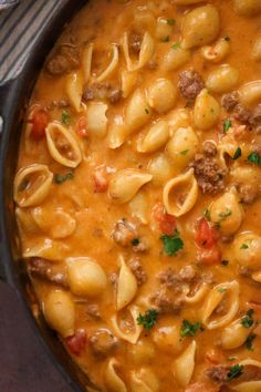 a pot filled with pasta and meat in tomato sauce on top of a wooden table