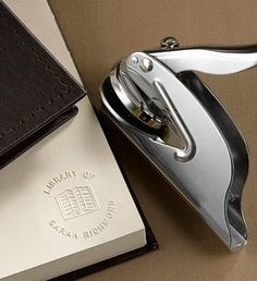 a silver lighter sitting next to an open book on top of a brown cloth covered table