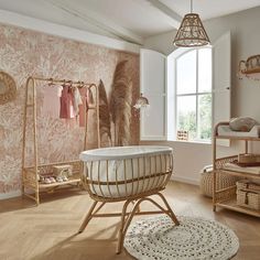 a baby's room with pink and white wallpaper, wicker crib, rattan chair, rugs and shelves