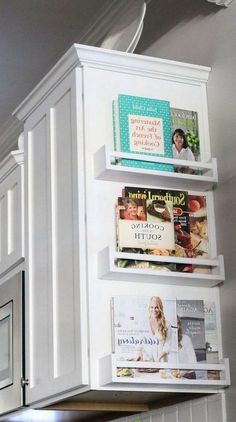 a kitchen with white cabinets and shelves filled with magazines on the wall above the stove