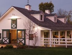 a white barn with green shutters and lights on the front door is lit up at night