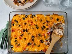 a casserole dish with cheese and olives on it, next to a plate of pizza