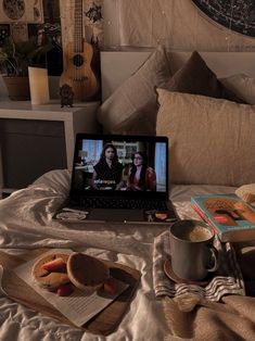 a laptop computer sitting on top of a bed next to a cup and saucer