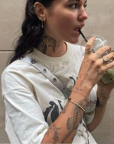 a woman with tattoos on her arm drinking from a cup and holding a straw in her hand