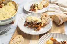 three plates with meat and cheese casserole next to bread on a cutting board