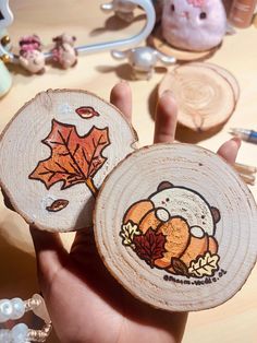 a person holding two wooden coasters decorated with autumn leaves and an animal on them