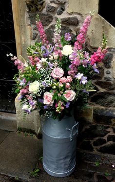 a bucket filled with lots of flowers sitting next to a stone wall