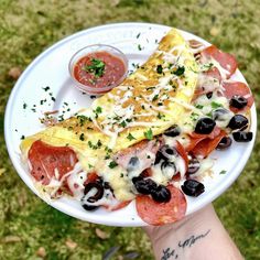 a person holding a plate with pizza and olives on it in their left hand