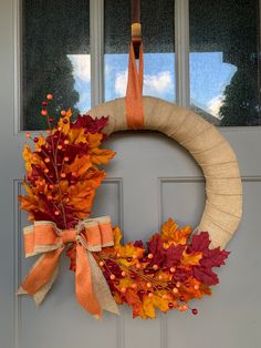 a wreath is hanging on the front door with fall leaves and oranges around it