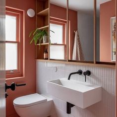 a white toilet sitting next to a bathroom sink under a mirror on top of a wall