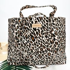 A large size leopard print bag with handles. Pictured on white background with palm leaf and straw hat. Reusable Travel Shoulder Bag, Reversible Bucket Travel Bag, Reversible Bucket Bag For Travel, Summer On-the-go Tote Beach Bag, Reusable Tote Shoulder Bag For Travel, Brown Reusable Travel Bags, Large Reusable Travel Bag, Rectangular Reusable Beach Bag For Travel, Reversible Tote Beach Bag For Travel