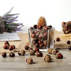 some nuts are sitting in a glass on a table next to a pine cone and purple flowers