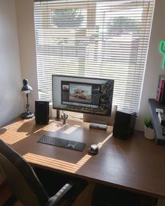 a desk with a monitor, keyboard and speakers in front of a window covered by blinds