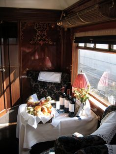 a table with wine bottles, bread and fruit on it in front of a window