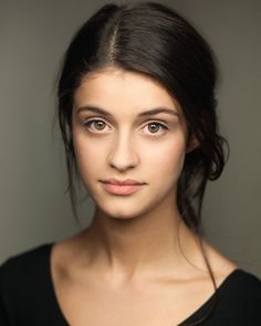 a beautiful young woman posing for a photo in front of a gray background with her hair pulled back