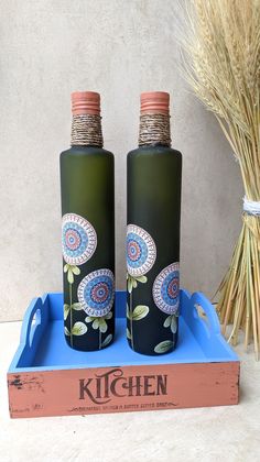 two green bottles sitting on top of a blue tray next to some dry grass and a dried plant