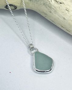 a sea glass pendant on a chain with a piece of driftwood in the background