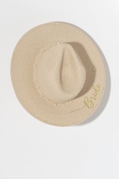 Keep the sunshine out of your eyes this summer with Shiraleah's "Bride" Pearl Hat. Made from natural paper straw with the word "Bride" embroidered in gold lettering along a pattern of faux pearls, this elegant beach hat is the perfect match to any honeymoon outfit. Pair with other items from Shiraleah's Hitched Collection to complete your look! Features a neutral straw color with a pattern of faux pearls and the word "bride" embroidered on the brim Shiraleah is a trend-driven lifestyle brand foc Pearl Hat, Pearl Bride, Honeymoon Outfits, Natural Paper, Gold Lettering, Beach Hat, Paper Straws, Gold Letters, A Pattern