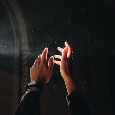 two hands reaching out towards each other in front of a dark room with light coming through the window