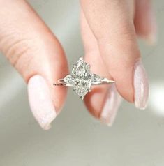 a woman's hand holding an engagement ring with two diamonds on it and the middle finger