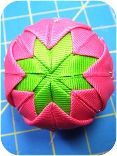 an origami ball with green and pink leaves on it sitting on a blue surface