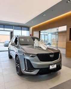 a silver car with a bow on the hood in a showroom filled with cars