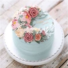 a blue cake with flowers on it sitting on a white plate next to a wooden table